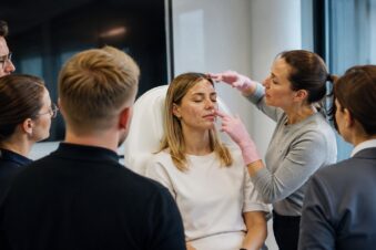 Botox-Kurs für Ärzte: mehrere Menschen stehen um eine Trainerin herum.